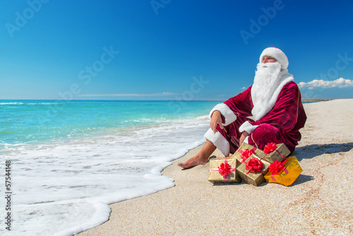 Santa Claus with many golden gifts relaxing at beach  - christma
