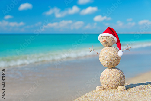 Sandy snowman in santa hat sunbathing in beach lounge. Holiday c
