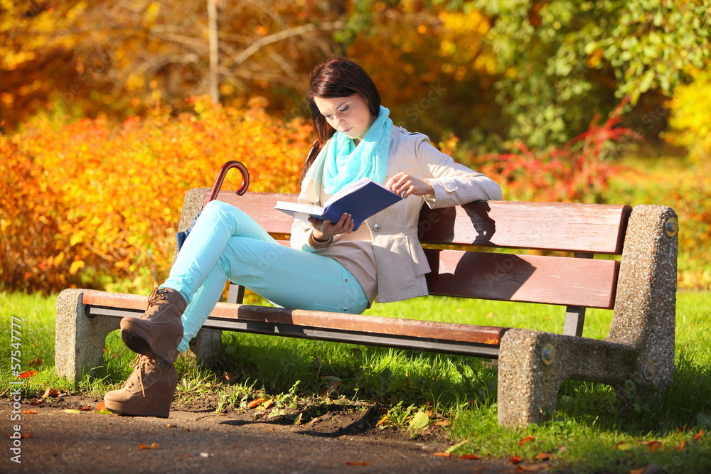 Young girl relaxing in autumnal park reading book