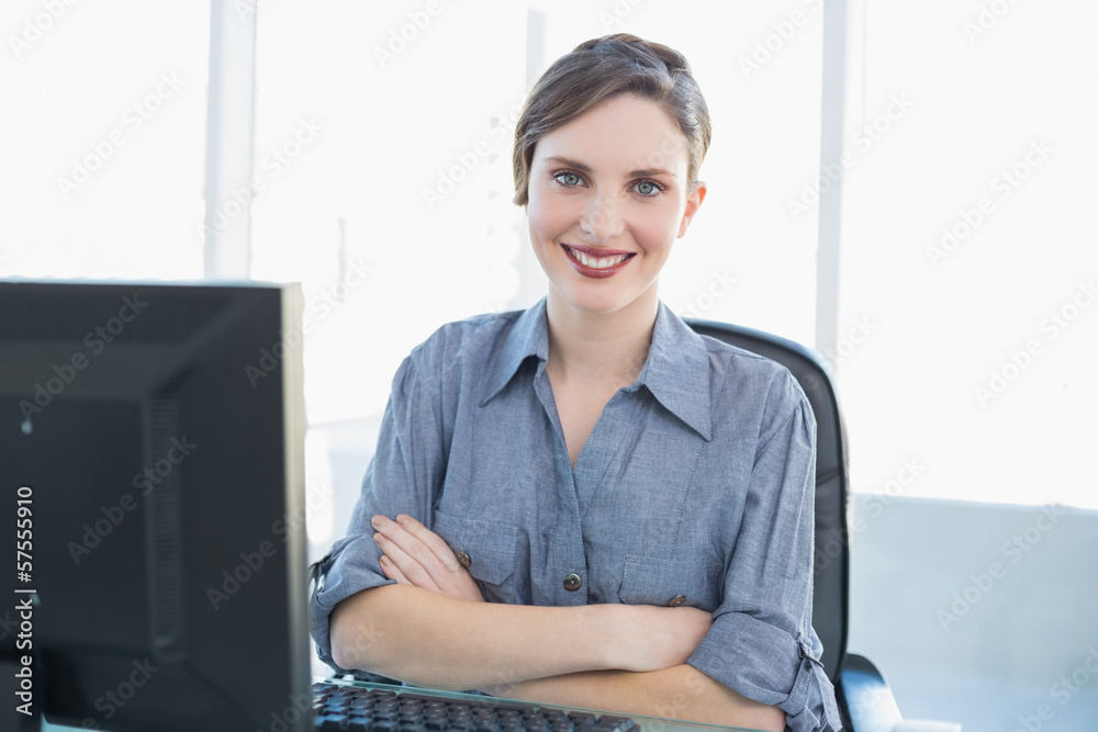 Cute young businesswoman sitting at her desk with arms crossed Cute young businesswoman sitting at her desk with arms crossed