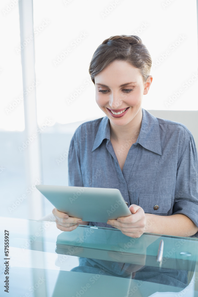 Cheerful young businesswoman using her tablet sitting at her des Cheerful young businesswoman using her tablet sitting at her des