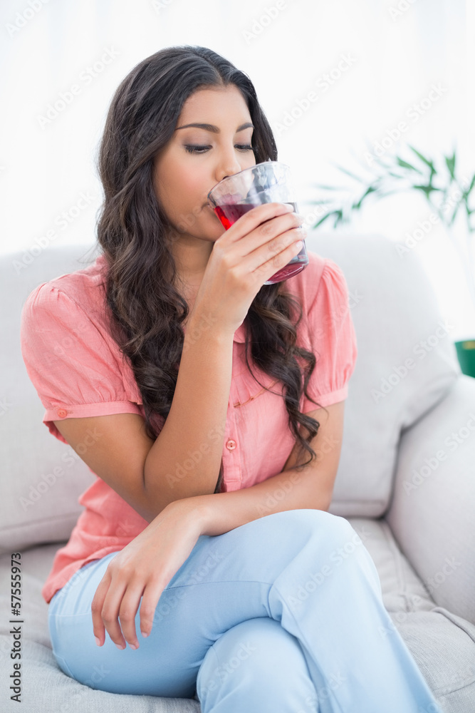 Calm cute brunette sitting on couch drinking glass of juice Calm cute brunette sitting on couch drinking glass of juice