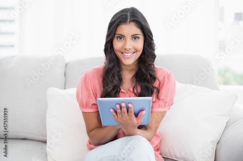 Happy cute brunette sitting on couch using tablet