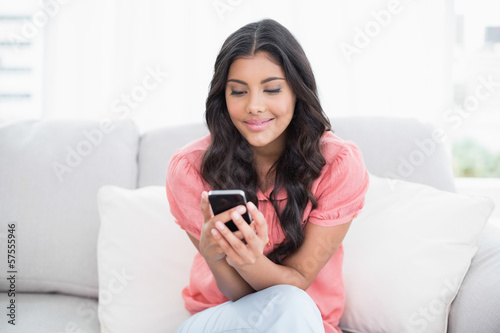 Content cute brunette sitting on couch holding smartphone