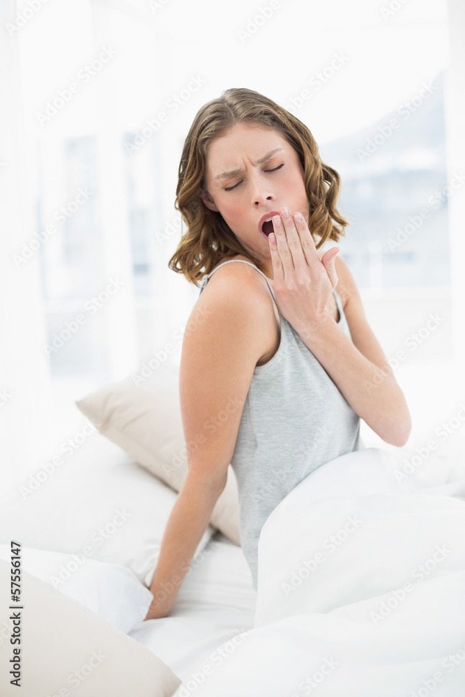 Pretty yawning woman sitting under the cover on her bed Pretty yawning woman sitting under the cover on her bed
