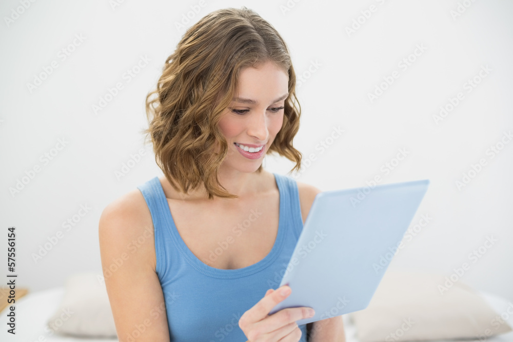 Cheerful cute woman using her blue tablet while sitting on her b Cheerful cute woman using her blue tablet while sitting on her b