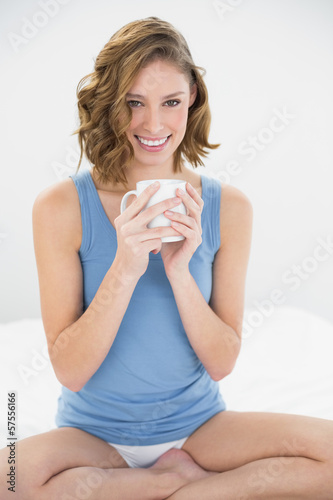 Calm woman sitting on her bed holding a white cup