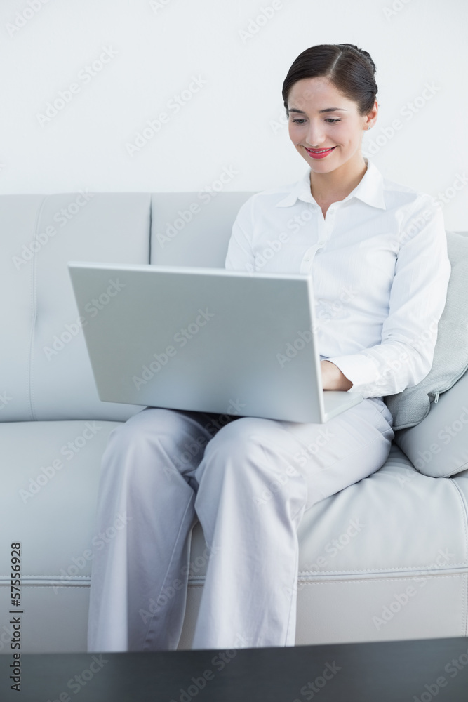 Smiling well dressed woman using laptop on sofa Smiling well dressed woman using laptop on sofa