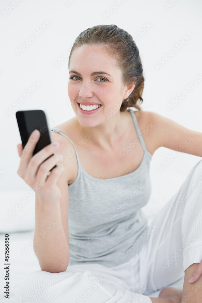 Smiling woman with mobile phone sitting in bed Smiling woman with mobile phone sitting in bed