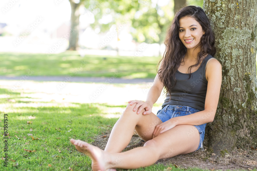 Casual attractive brunette sitting leaning against tree Casual attractive brunette sitting leaning against tree
