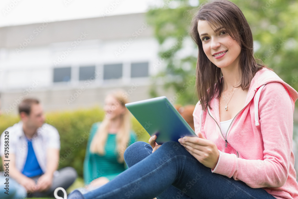 Fototapeta premium Smiling college girl using tablet PC with students in park
