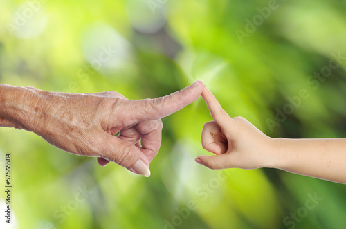 Senior's hand touching a child's hand on green nature background photo