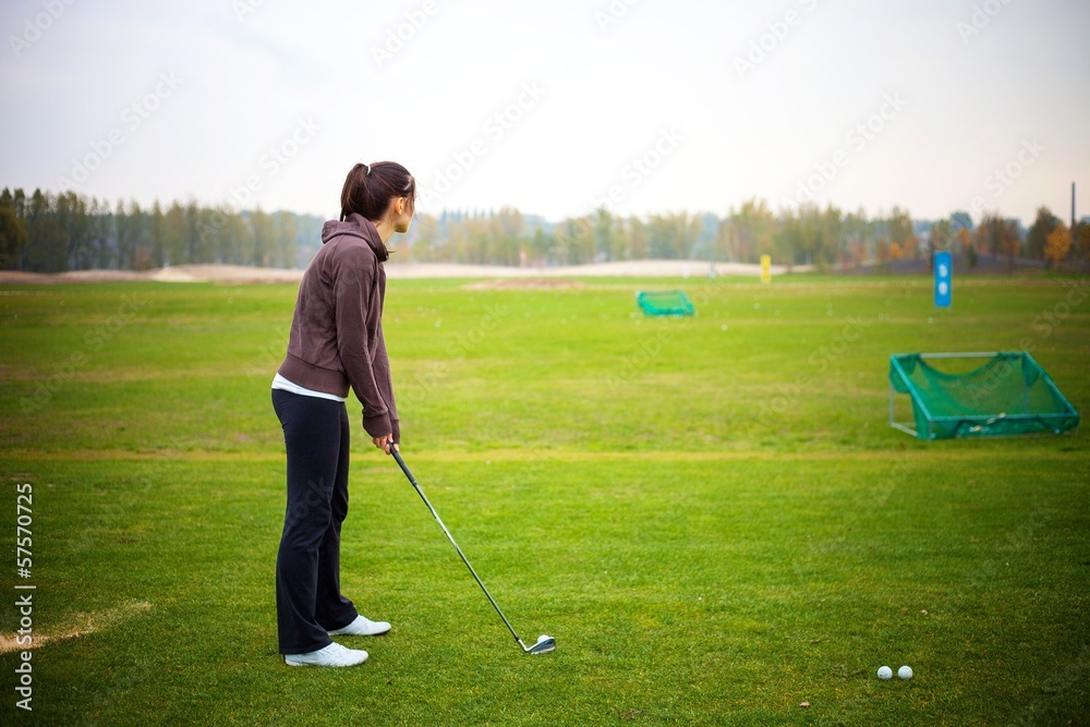 Obraz premium Young woman training golf at the driving range