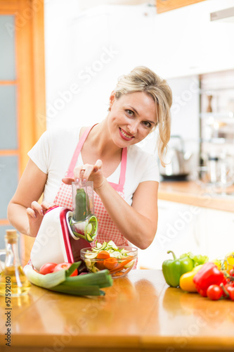 Cute woman cutting vegetables with device at the kitchen table