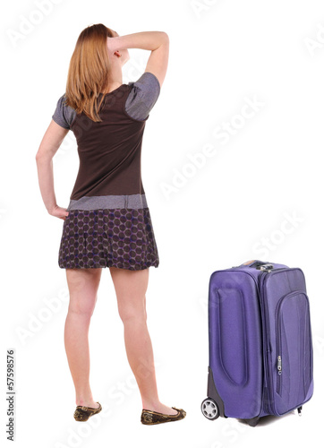 Beautiful young woman traveling with suitcas and looking at wall