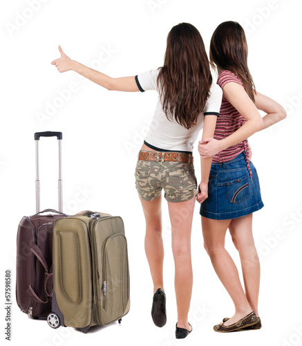 Two young women friends traveling with suitcas and showing thum