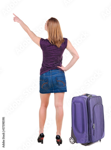 Beautiful young woman in dress traveling with suitcas and point