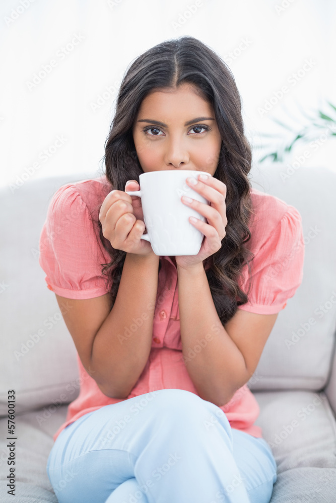 Calm cute brunette sitting on couch holding mug