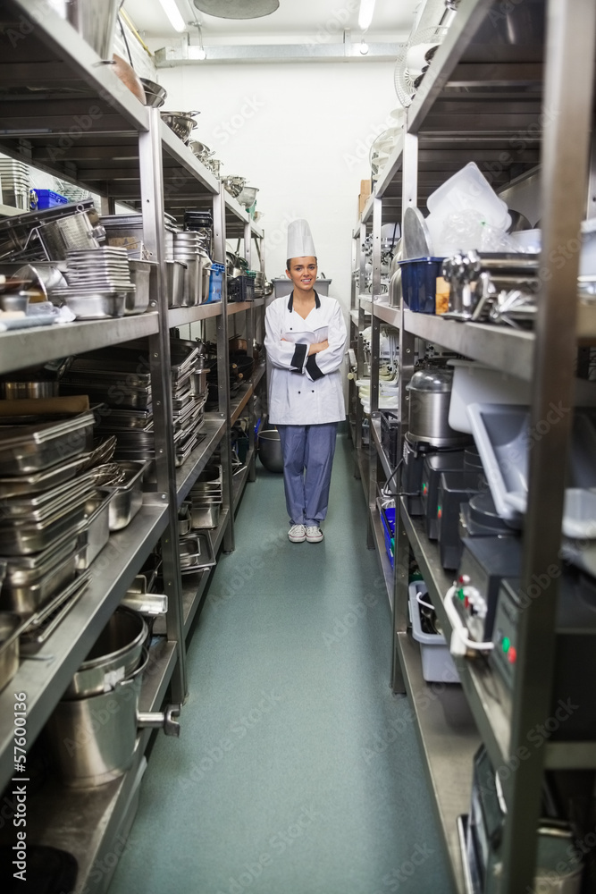 Young pretty chef standing arms crossed between shelves