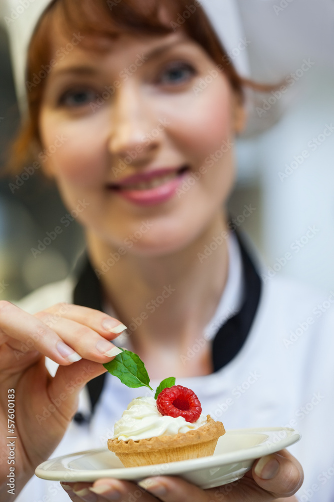 Pretty head chef putting mint leaf on little cake on plate Pretty head chef putting mint leaf on little cake on plate
