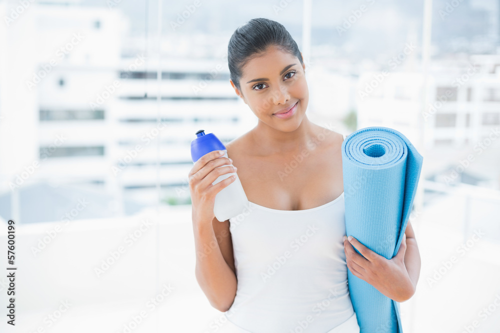 Pleased toned brunette holding sports bottle and exercise mat Pleased toned brunette holding sports bottle and exercise mat