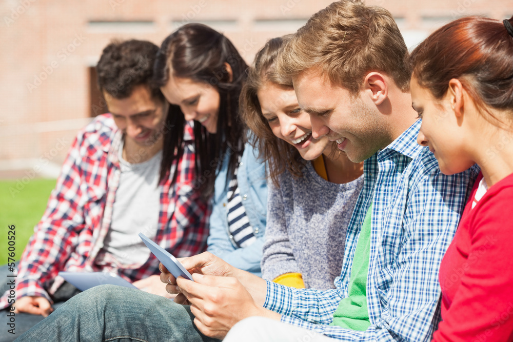 Five smiling students sitting on the grass using tablet Five smiling students sitting on the grass using tablet