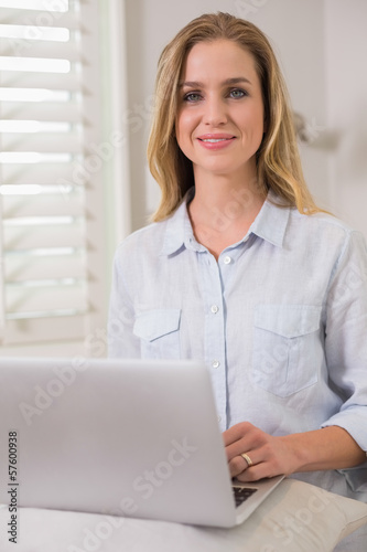 Content casual blonde sitting on couch using laptop