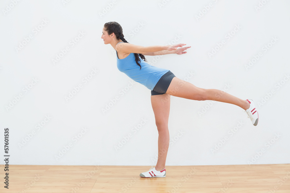Full length of a woman standing on one leg in fitness center