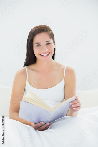 Portrait of a smiling woman with book in bed
