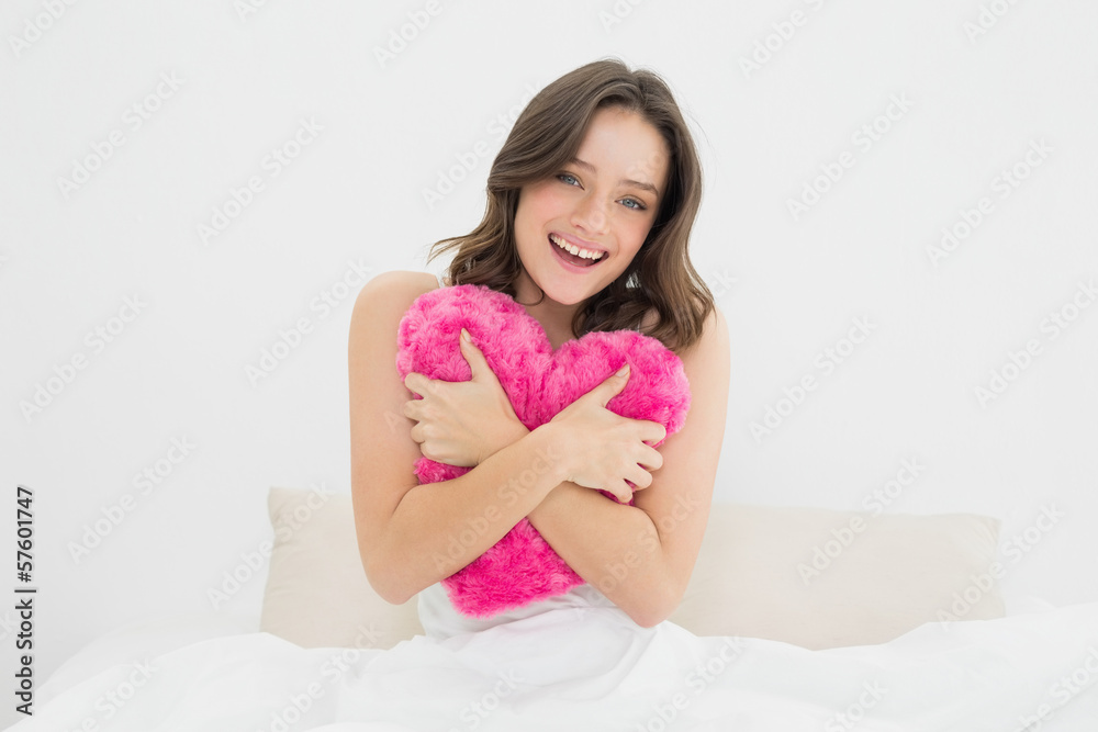 Happy woman hugging heart shaped pillow in bed Happy woman hugging heart shaped pillow in bed