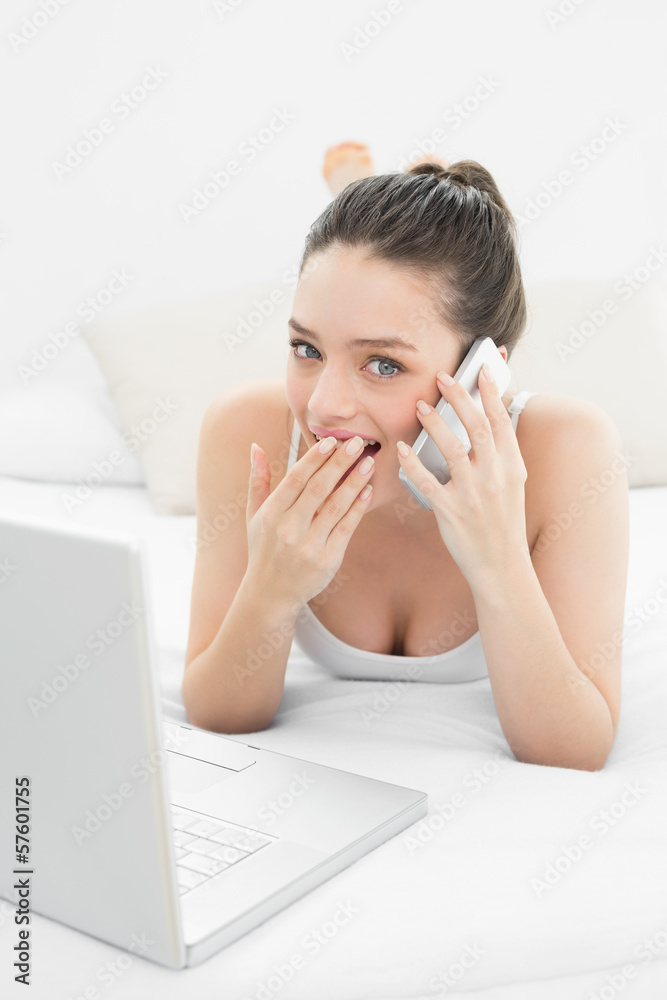 Shocked woman using cellphone and laptop in bed Shocked woman using cellphone and laptop in bed