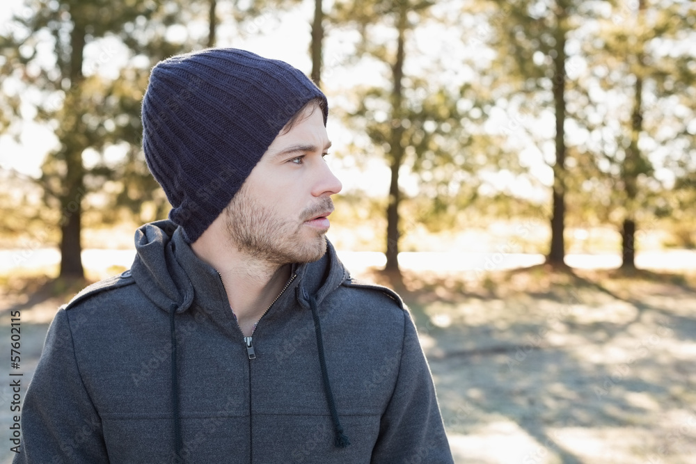 Young man in warm clothing looks to his side in forest Young man in warm clothing looks to his side in forest