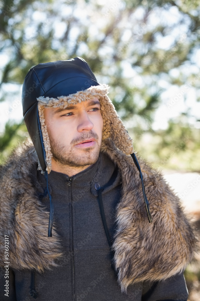 Young man in warm clothing looks to his side in forest Young man in warm clothing looks to his side in forest
