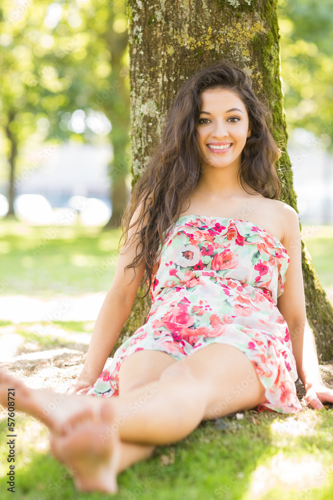 Stylish smiling brunette sitting and leaning against tree Stylish smiling brunette sitting and leaning against tree