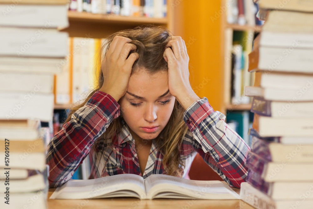 Irritated pretty student studying between piles of books Irritated pretty student studying between piles of books