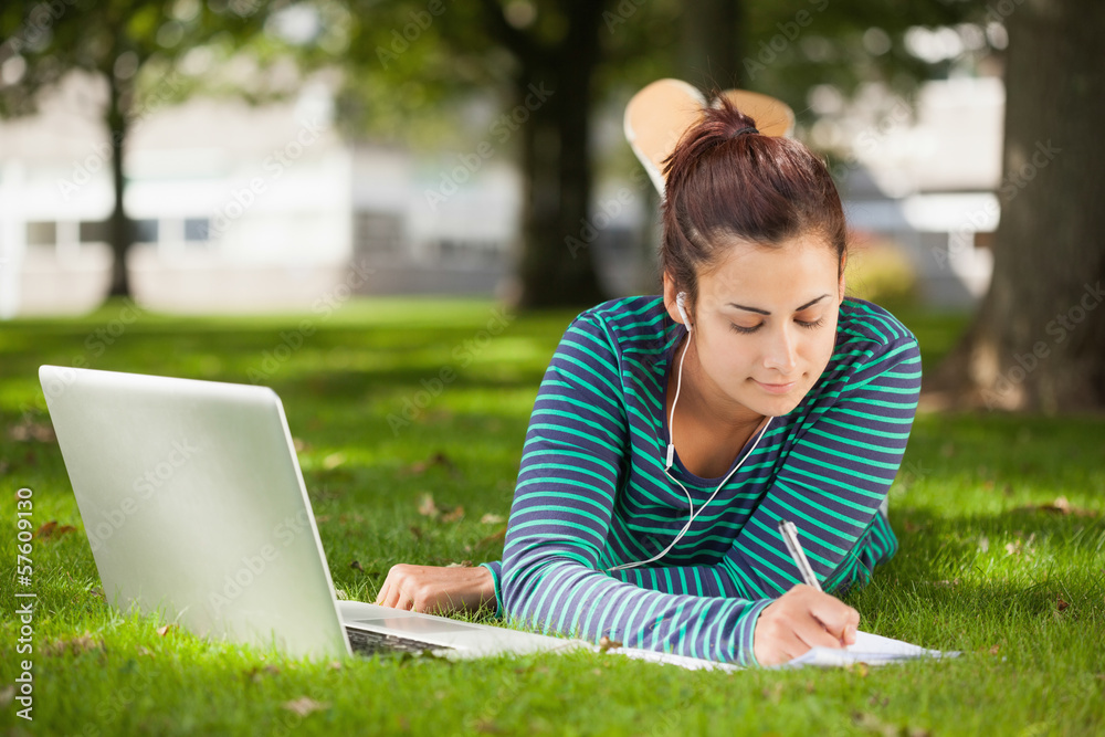 Calm casual student lying on grass taking notes Calm casual student lying on grass taking notes