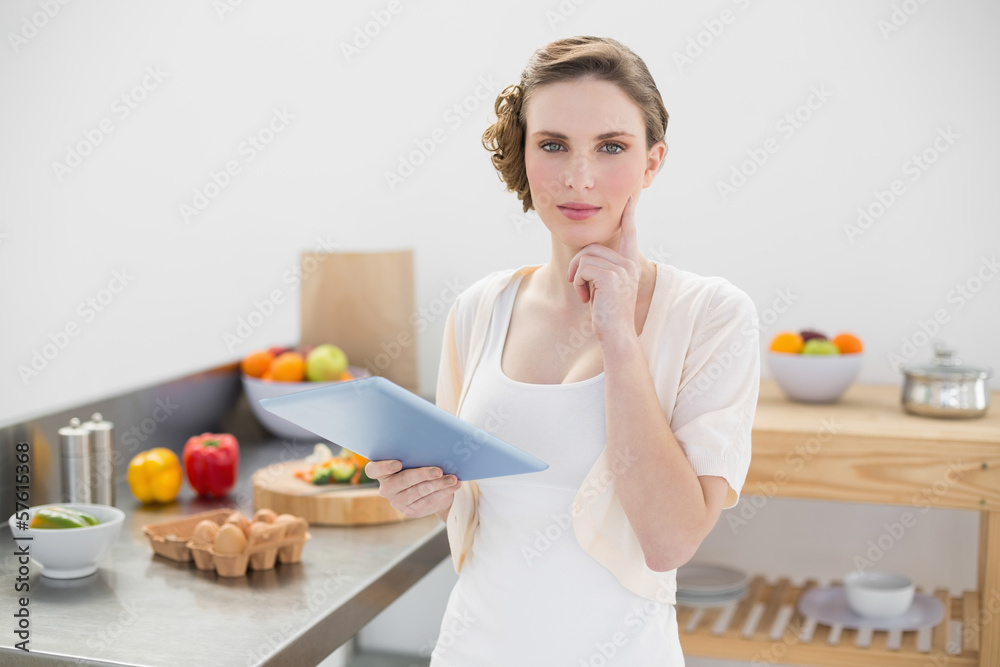 Thinking gorgeous woman standing in kitchen while holding her ta