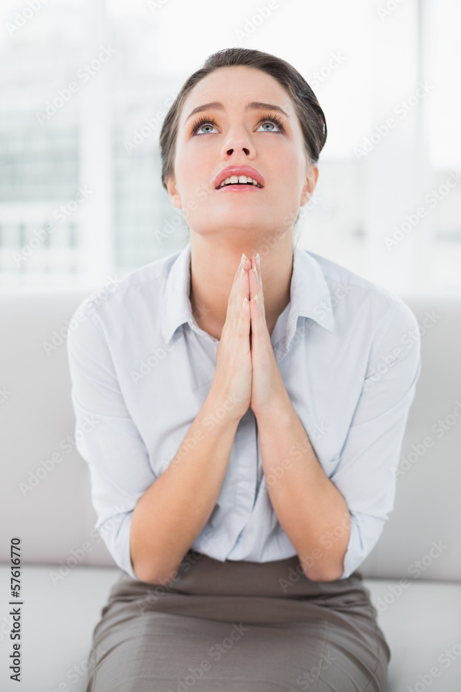 Worried well dressed woman with joined hands looking up