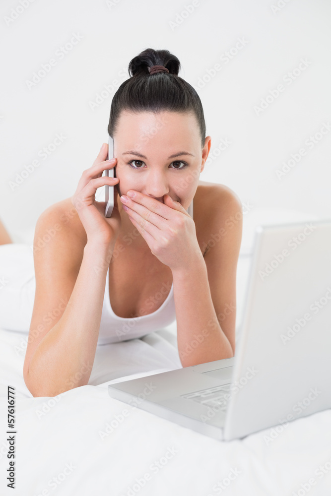 Shocked casual woman using cellphone and laptop in bed Shocked casual woman using cellphone and laptop in bed