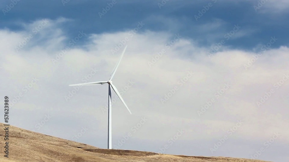 Single wind turbine turning on hillside with blue sky and clouds Single wind turbine turning on hillside with blue sky and clouds