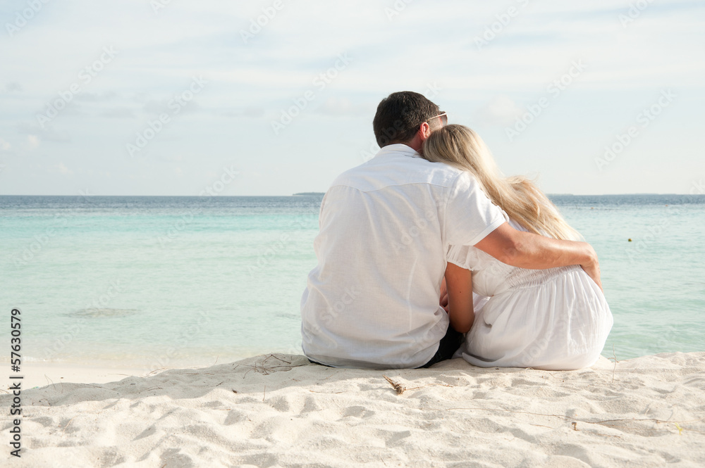 couple sittng on sand facing ocean