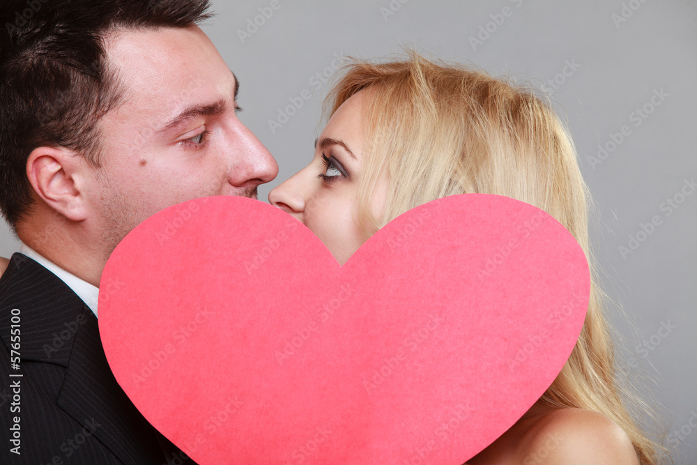 happy bride and groom kissing behind red heart