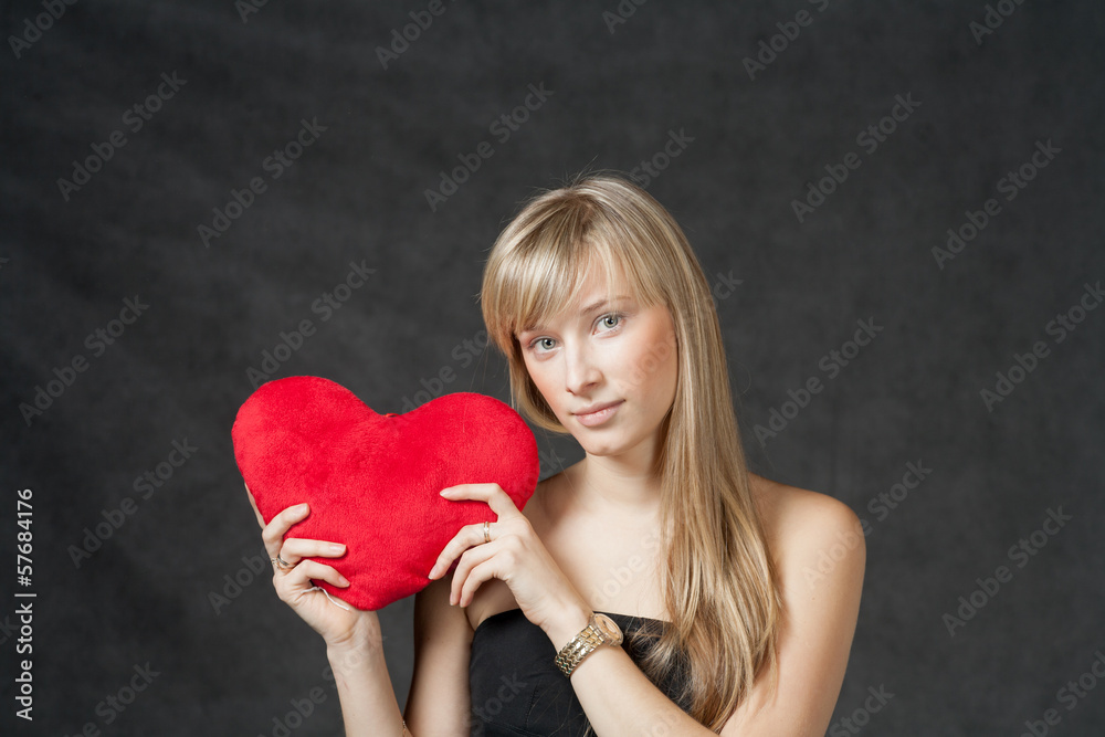 American Blond haired Woman with a Heart-Shaped Cushion on dark American Blond haired Woman with a Heart-Shaped Cushion on dark