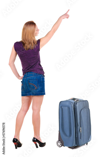 Beautiful young woman in dress traveling with suitcas and point