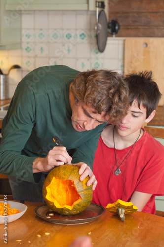 father and son carving Halloween pumpkin on a kitchen table