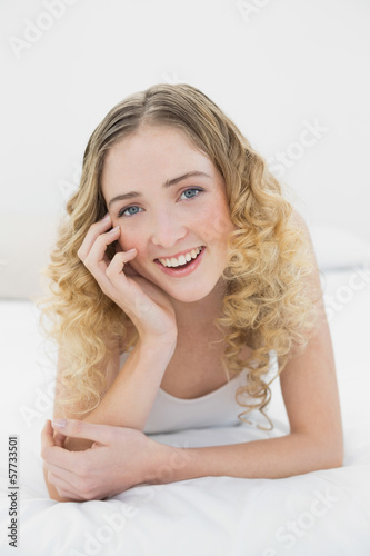 Pretty smiling blonde lying on bed looking at camera