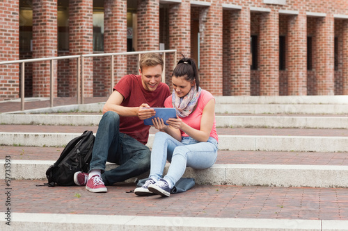 Happy students sitting on stairs using tablet