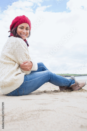 Smiling woman in stylish warm clothing sitting on beach