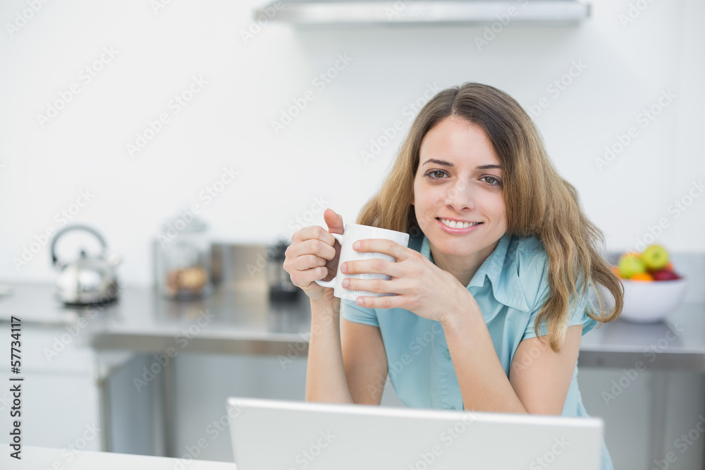 Cheerful smiling woman holding a cup posing in her kitchen Cheerful smiling woman holding a cup posing in her kitchen