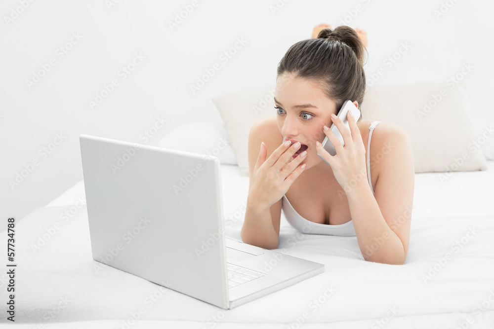 Shocked woman using cellphone and laptop in bed Shocked woman using cellphone and laptop in bed